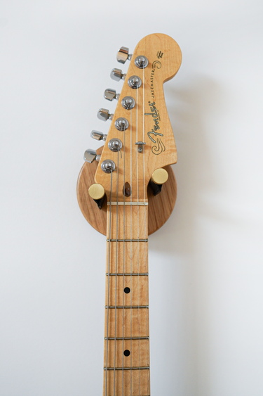Close-up of a Fender electric guitar headstock and upper neck mounted on a wooden guitar hanger against a plain white background.
