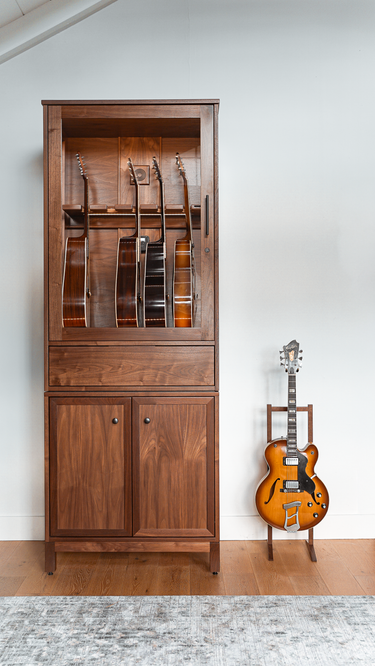 a guitar humidor cabinet with built in pedal board storage below next to a wooden single guitar stand