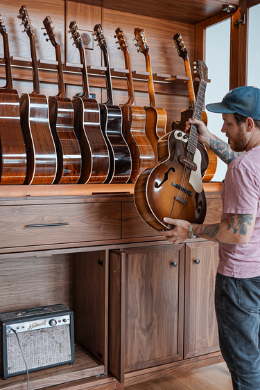 a man in a music room with a guitar display cabinet with a guitar amp below in a storage section