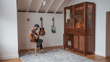 a man in a music room playing an electric guitar plugged into a guitar display case